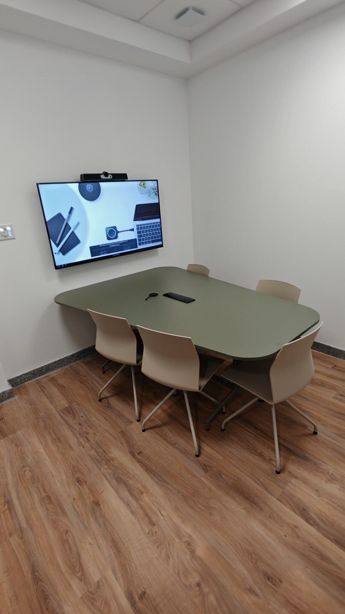 Petite salle de réunion : écran, barre de visioconférence et bouton de partage sans fil posé sur la table.