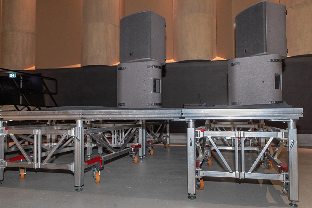 Enceintes posées sur un plateau de scène monté sur structure.