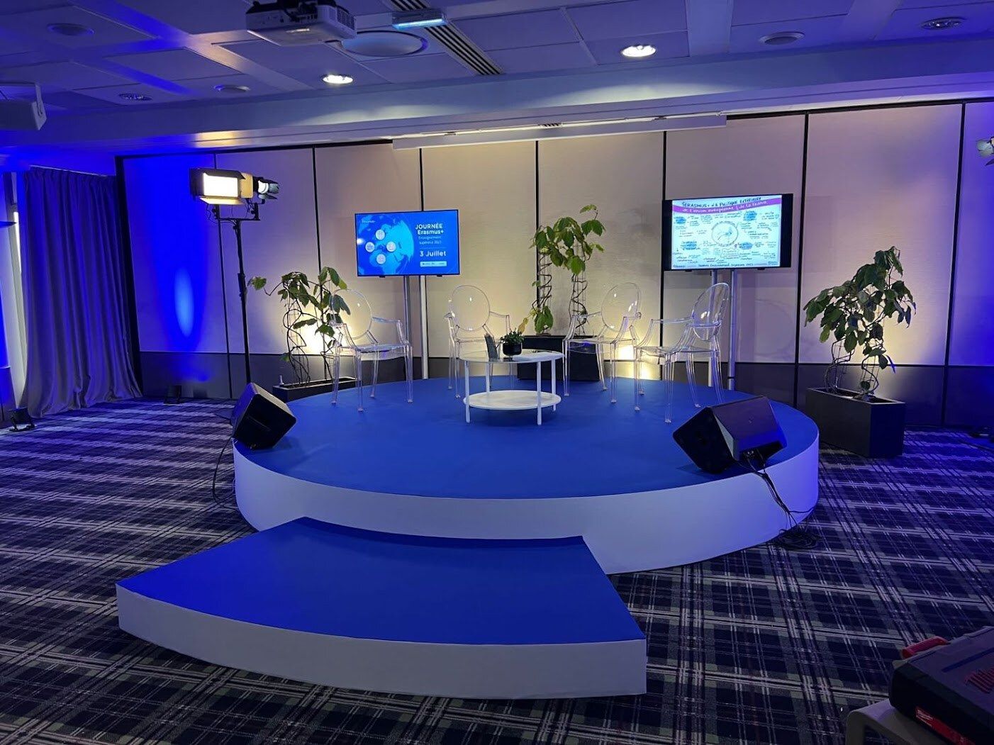 Journée Erasmus+ : plateau rond, écrans de part et d’autre et mise en lumière bleue de la salle.