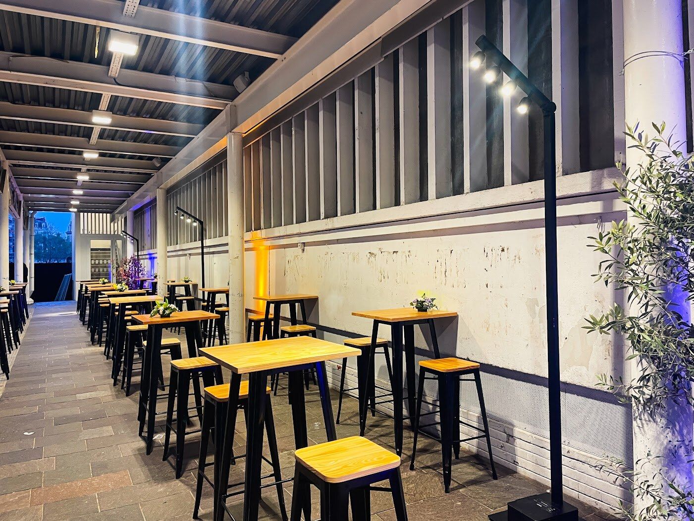 Cocktail sous la halle : mange-debout et éclairage d’ambiance sur mâts, ambre et bleu.