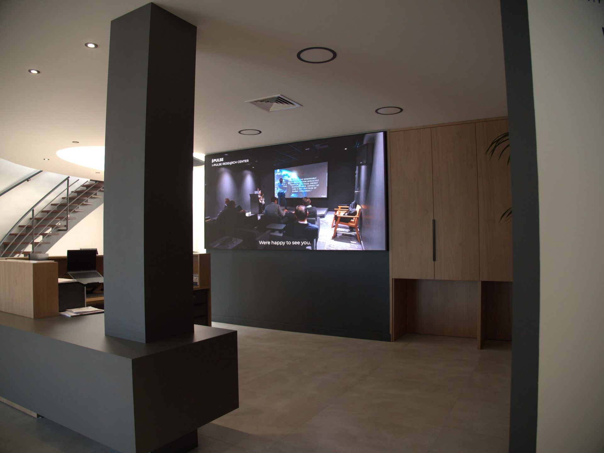 Le même hall vu depuis l’escalier : l’écran est intégré au mobilier d’accueil.