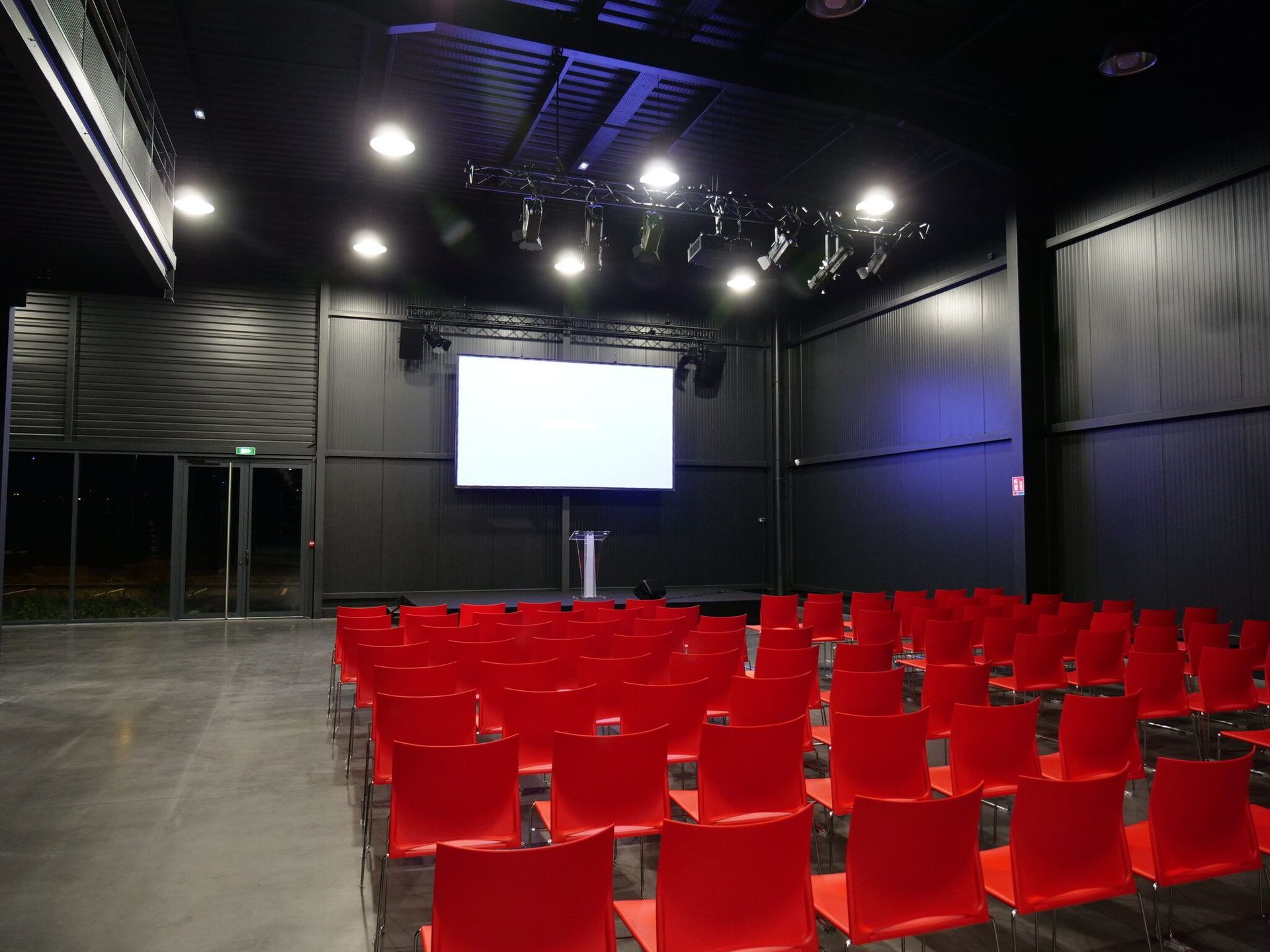 Salle événementielle en configuration conférence : gradin, écran et éclairage de salle.